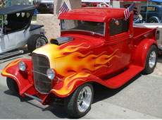 A show truck with American flags hanging from its windows is displayed at the car show.