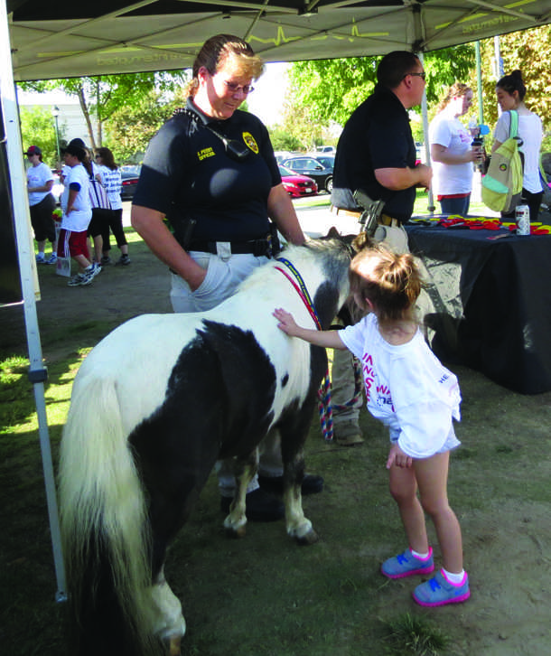 Kaitlynn Tackett, 2, is seen petting Macho, a miniature horse, with Officer Sonja Peery at a Life Interrupted booth set up at the 2nd annual Walk Like MADD event.