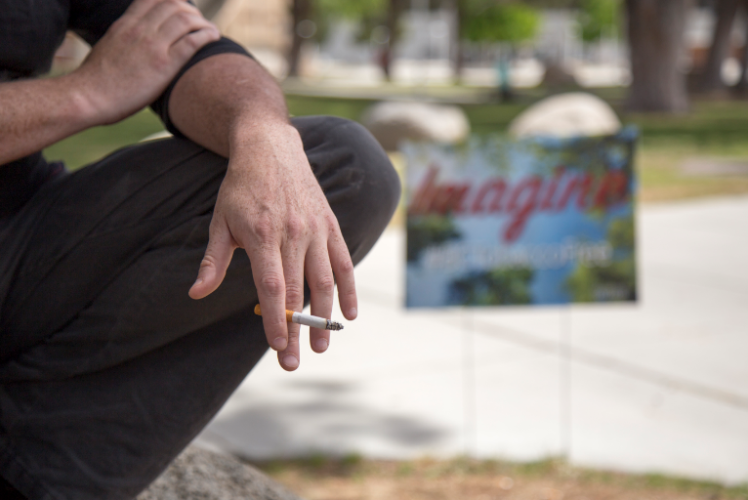 A student smokes while posing near “BCTobaccoFree” ad.
