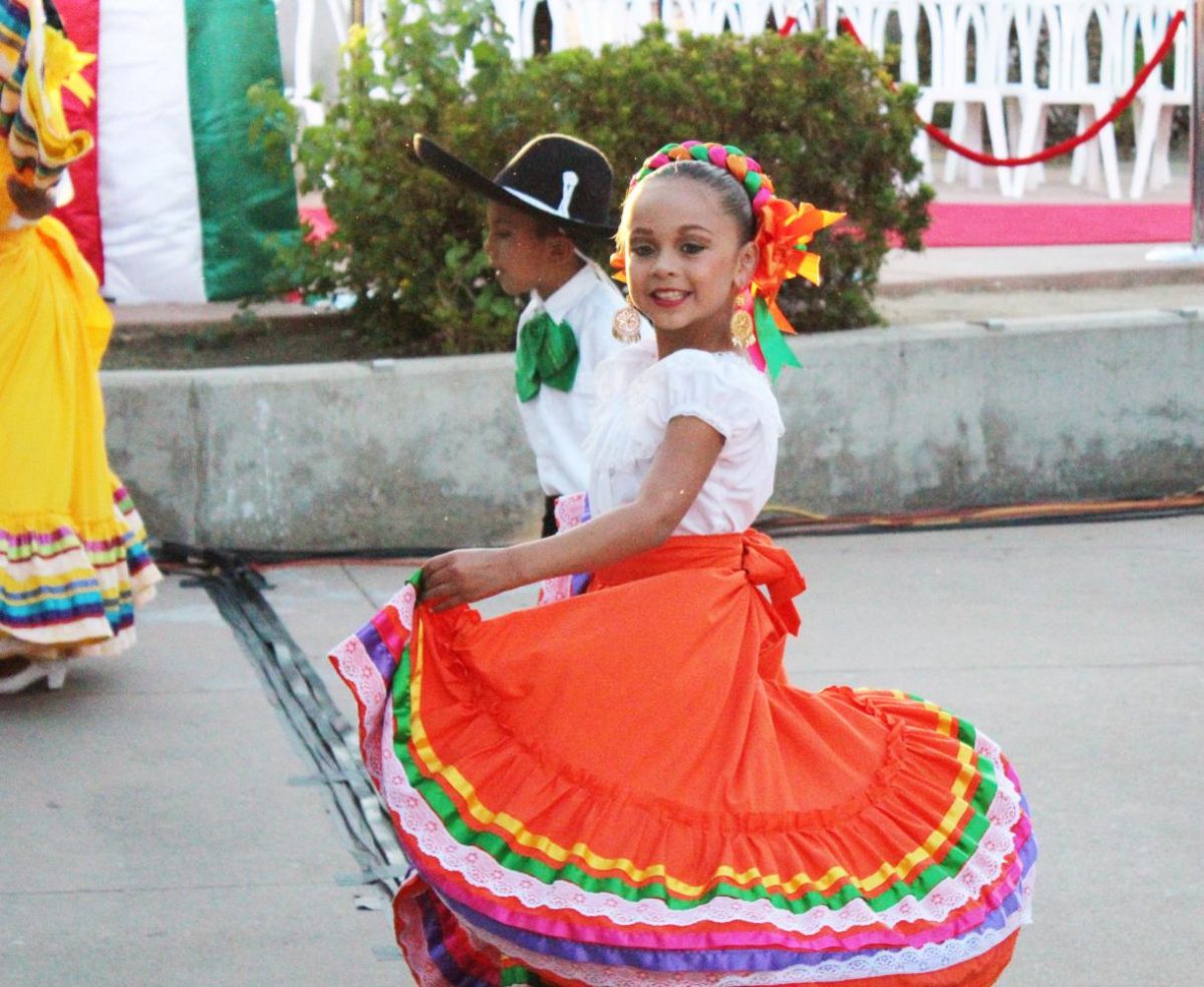 A little girl smiles as she twirls her skirt during a traditional Mexican dance routine.
