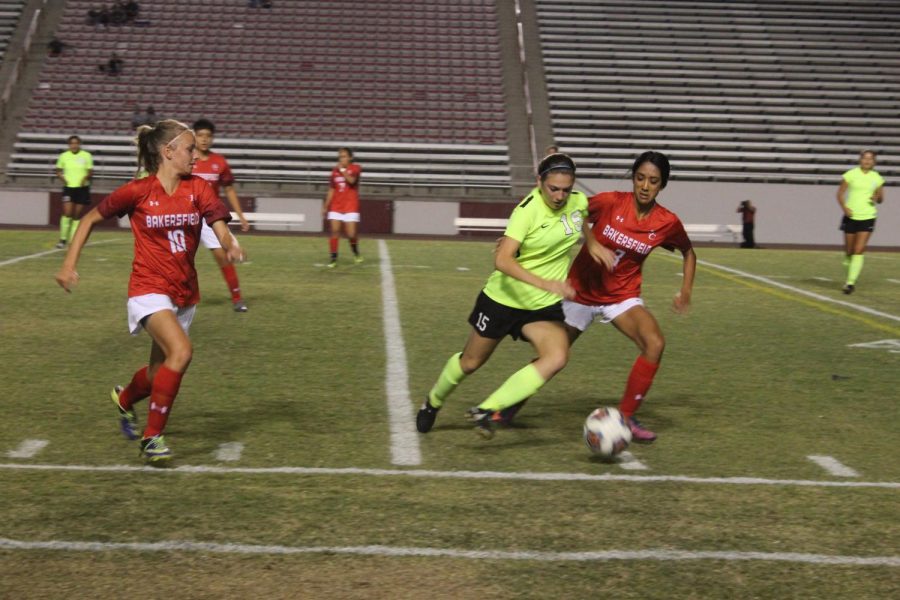 Alexia Raudier (left) and Jackie Garcia (far right) put pressure on VC player Paola Gonzales in attempt to steal the ball.