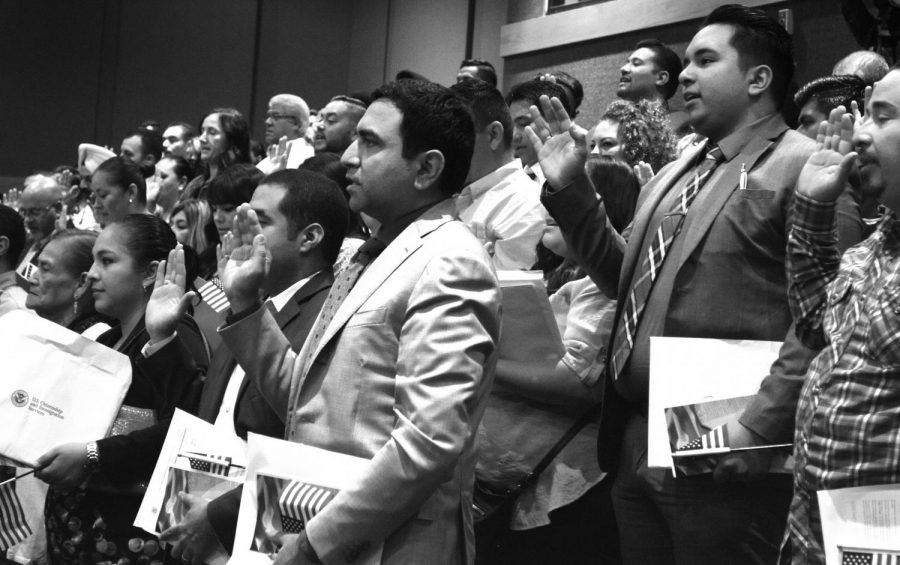 131 people raise their right hands as they swear the Oath of Allegiance and become naturalized citizens at the library.