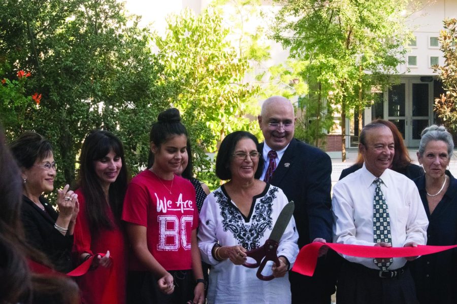 several people pose while woman in center cuts ribbon with a large scissors