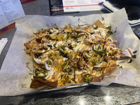 A serving of nachos with cheeses sauces and meats on it on top of parchment paper in a serving dish