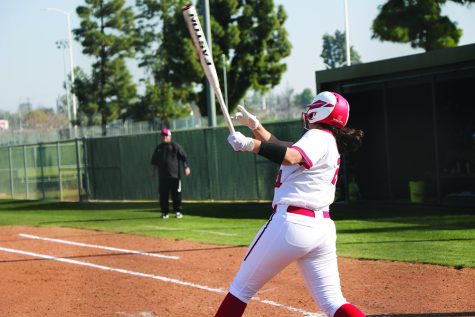 woman in white uniform with read and white cap with bat in motion