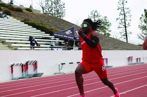 Black man wearing read running uniform running on track.