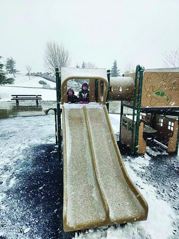Scott Steele’s children enjoying the snow at Warrior Park. HIs kids are on top of a snowy slide in their snow gear on a playground.